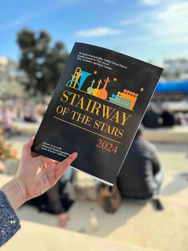 A photo of a person holding a closed concert program booklet which reads Stairway of the Stars 2024 on the cover.